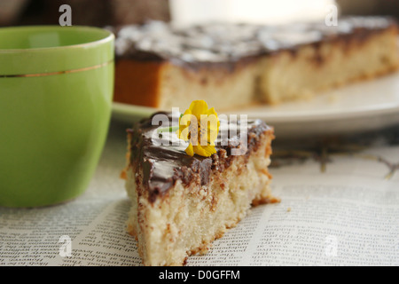 Une tranche de banane chocolat gâteau décoré avec une fleur jaune se place sur un journal. Banque D'Images