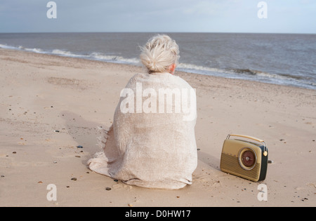 Woman sitting on beach enveloppée dans un châle Banque D'Images