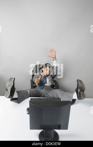 Businessman gesturing avec ses pieds jusqu'à l'avant d'un PC de bureau Banque D'Images