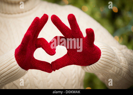 Pull femme avec des mitaines rouges tendent un Cœur signe avec ses mains. Banque D'Images