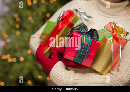 Femme portant un chandail et les mitaines rouges contre un fond doré et vert abstrait Holding Christmas Gifts Banque D'Images