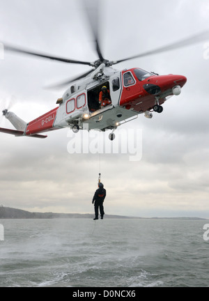 L'hélicoptère des garde-côtes sur un treuillage terne et jour de tempête Banque D'Images