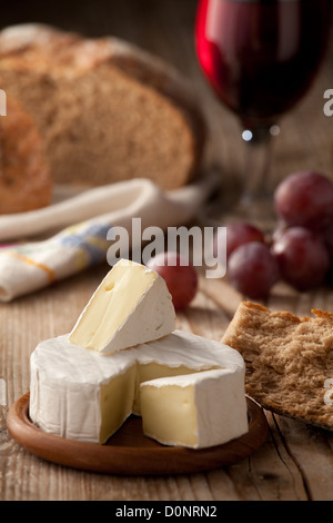 Pièce et roue de fromage Camembert de Normandie traditionnel comprenant du pain, du raisin et un verre de vin rouge sur la table en bois Banque D'Images