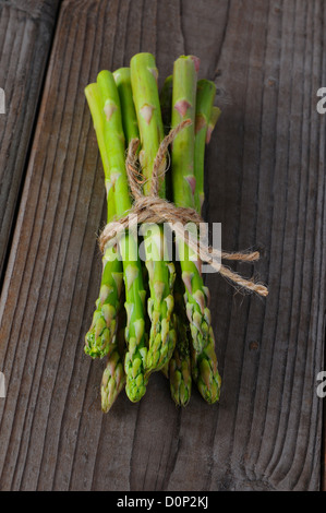 Un bouquet d'asperges attachées avec de la ficelle sur un fond de bois rustique. Format vertical. Banque D'Images