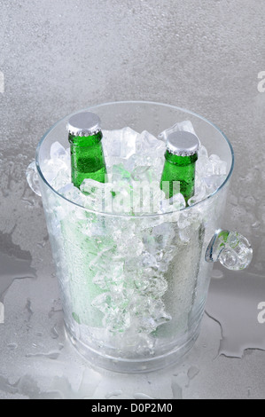 Deux bouteilles de bière verte dans un seau à glace en cristal assis sur une surface en acier inoxydable. Banque D'Images