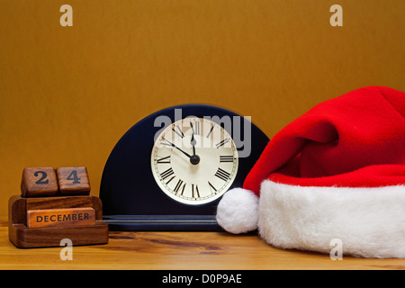 Une table de salle de réveil montre qu'il est près de minuit la veille de Noël, avec 24 Calendrier et Santa Claus hat. Banque D'Images