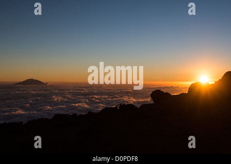 Le mont Kilimandjaro, Tanzanie - Le sommet du Mont Meru pokes à travers les nuages que le soleil se couche à l'horizon comme vu à partir de la flèche située sur le glacier du Kilimandjaro Lemosho Route. Banque D'Images