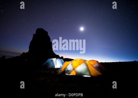 Le mont Kilimandjaro, Tanzanie - tentes au Lava Tower Camp de nuit, avec des étoiles. La formation rocheuse à gauche est la silhouette de Lava Tower. Le soleil n'a que récemment disparu sous l'horizon et est encore partiellement illuminant le ciel très bas. Banque D'Images