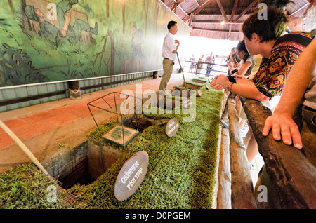 HO CHI MINH-VILLE, Vietnam — Un guide explique divers dispositifs antipersonnel sur le site historique des tunnels de Cu Chi, démontrant les mesures défensives utilisées pendant la guerre du Vietnam. L'exposition présente différents types de pièges qui protègent le réseau de tunnels et la zone environnante. Ces artefacts militaires préservés font partie des expositions éducatives du site sur les tactiques défensives vietnamiennes. Banque D'Images