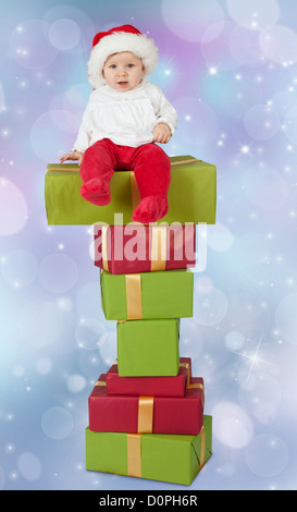 Bébé assis sur une pile de cadeaux de noël, isolé sur un arrière-plan flou bleu Banque D'Images