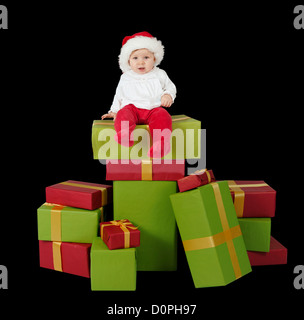 Bébé assis sur une pile de cadeaux de noël, isolé sur fond noir Banque D'Images