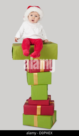 Bébé assis sur une pile de cadeaux de noël, isolé sur fond gris Banque D'Images