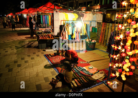Vendeur du marché de nuit Quai Fa Ngum Vientiane Laos // VIENTIANE, Laos — Une vendeuse et sa fille s'occupent de leur étal au marché de nuit le long du quai Fa Ngum sur les rives du Mékong à Vientiane. Le marché de nuit opère le long de cette promenade riveraine, qui est parallèle au Mékong et sert d'une des principales zones de rassemblement commercial et social de Vientiane. Le quai Fa Ngum, nommé d'après le fondateur du Royaume lao, s'étend le long de la limite ouest de la capitale. Le marché présente généralement des vendeurs locaux vendant de la nourriture, de l'artisanat et des marchandises aux résidents et aux visiteurs. Vientia Banque D'Images