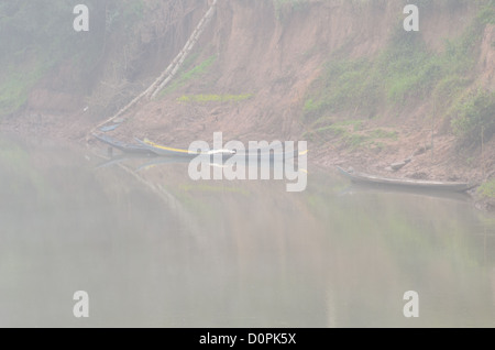 Bateaux en bois rivière Nam Tha Luang Namtha Laos // LUANG NAMTHA, Laos — les brumes du matin enveloppent des bateaux en bois positionnés le long de la rive de la rivière Nam Tha dans la province de Luang Namtha, dans le nord du Laos. La rivière Nam Tha sert de voie navigable vitale à travers cette région montagneuse près des frontières avec la Chine et le Myanmar. La province de Luang Namtha est connue pour ses diverses communautés ethniques et sert de porte d'entrée à la zone protégée nationale de Nam Ha. La région est devenue de plus en plus importante pour l'écotourisme et le transport fluvial. Les bateaux traditionnels en bois restent essentiels pour le transport local A. Banque D'Images