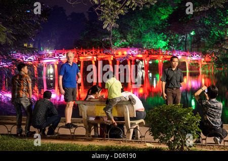 HANOI, Vietnam — les touristes posent pour des photos sur les rives du lac Hoan Kiem devant le pont Huc (pont du soleil du matin) la nuit. Le pont en bois peint en rouge relie la rive nord du lac à l'île de Jade et au temple de la montagne de Jade (temple Ngoc son). Banque D'Images