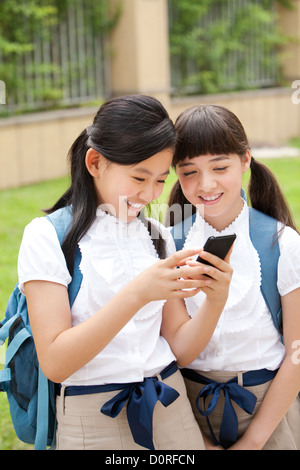 Ecolières excité en uniforme avec smart phone en cour de l'école Banque D'Images