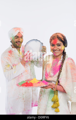 Homme jouant d'un tambourin avec une femme tenant un plateau de couleurs Holi Banque D'Images