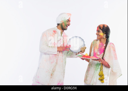 Homme jouant d'un tambourin avec une femme tenant un plateau de couleurs Holi Banque D'Images