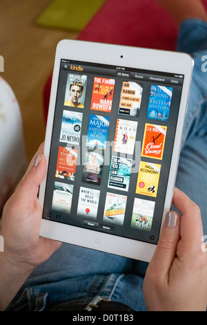 Femme à l'aide de l'application Kindle lire la sélection d'e-books en bibliothèque sur un ordinateur tablette iPad mini Banque D'Images