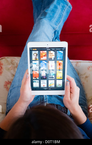 Femme à l'aide de l'application Kindle lire la sélection d'e-books en bibliothèque sur un ordinateur tablette iPad mini Banque D'Images