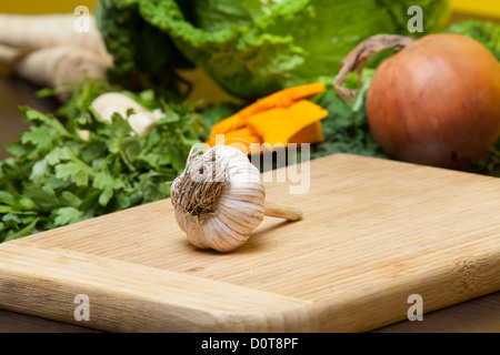 Ensemble d'ail allongé sur une planche en bois à côté d'autres légumes frais prêts à être utilisés comme ingrédients dans la cuisine Banque D'Images