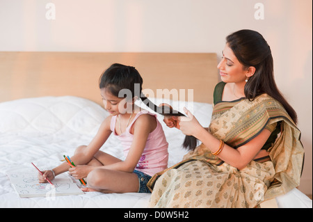 Femme peigner les cheveux de sa fille à faire leurs devoirs Banque D'Images