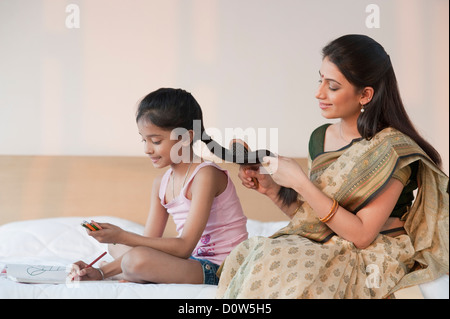 Femme peigner les cheveux de sa fille à faire leurs devoirs Banque D'Images