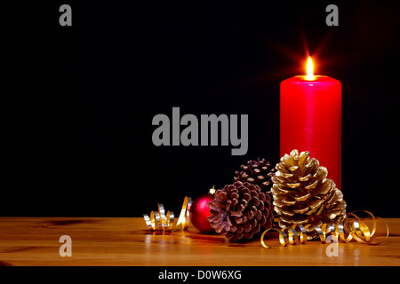 Still Life photo d'une bougie de Noël lumineux brûlant avec des pommes de pin d'or et ruban plus une babiole rouge Banque D'Images