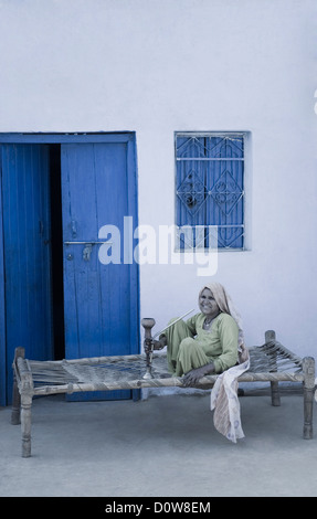 Femme fumant un narguilé sur un lit, Farrukh Nagar, Gurgaon, Haryana, Inde Banque D'Images