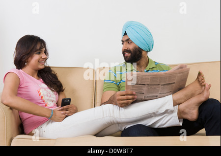 Homme Sikh lire un journal et d'une femme la messagerie texte sur un téléphone mobile Banque D'Images