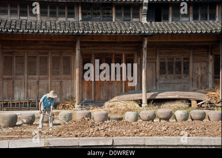 Un agriculteur travaillant en face d'une vieille maison en bois chinois Banque D'Images