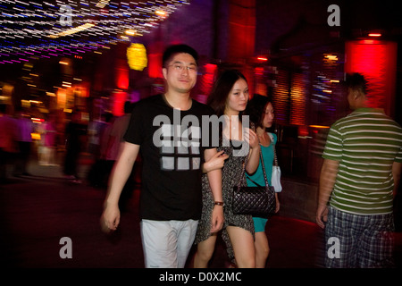 Un couple en train de marcher bras dessus, bras dessous au-delà d'un bar au bord de l'eau sur la rue Shichahai Lotus (marché), Beijing, Chine. Banque D'Images