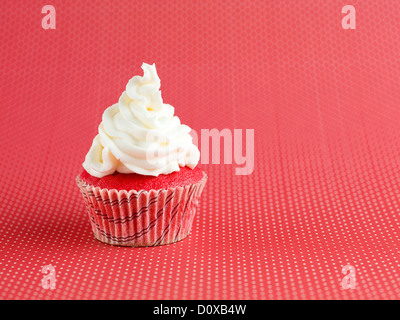 Libre d'un seul petit velvet cupcake, avec glaçage blanc sur le dessus, isolé sur fond pois rouge Banque D'Images