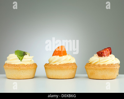 Trois délicieuses tartelettes aux fraises kiwi abricot fond dégradé neutre Banque D'Images
