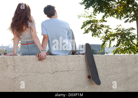 Young couple sitting on wall holding hands Banque D'Images