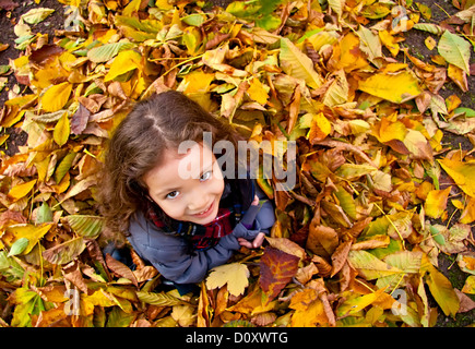 Petite fille assise sur un tas de feuilles jaunes Banque D'Images