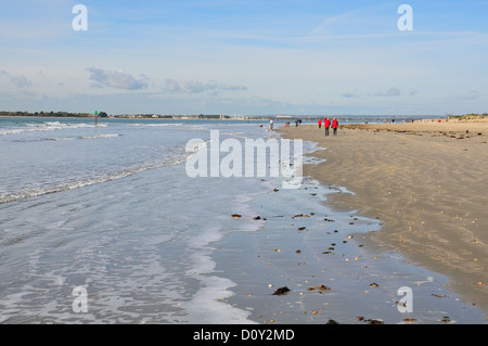 Scène de gens se promener le long de l'estran de la plage de West Wittering, nr Chichester, West Sussex.Hayling Island dans la distance Banque D'Images