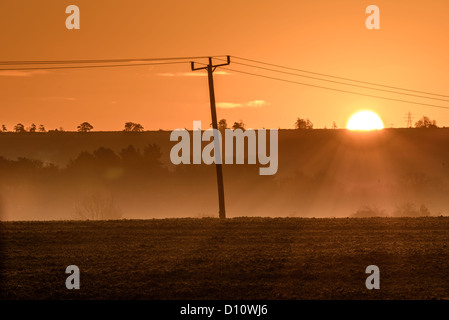 Lever du soleil sur une colline lointaine avec brouillard passant de près de la terre. Un poteau télégraphique et fils à la géométrie pour la scène Banque D'Images