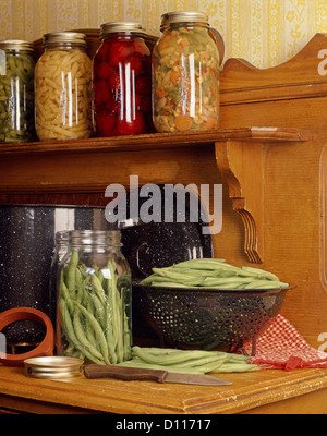 Comptoir de cuisine en bois vintage avec les haricots verts dans une passoire et les bocaux de conserves de légumes Banque D'Images