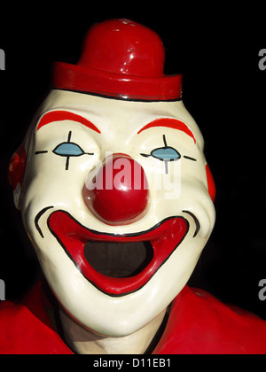 Riant visage blanc de clown sideshow avec nez rouge, la bouche et le chapeau - sur un fond noir Banque D'Images