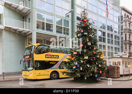 Passage bus touristique Checkpoint Charlie avec un arbre de Noël décoré de drapeaux internationaux à Berlin Allemagne Banque D'Images