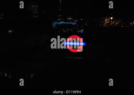 London Underground tube lumineux, signe avec fond sombre pour copier l'espace. Des lueurs de la ville la nuit derrière. Banque D'Images