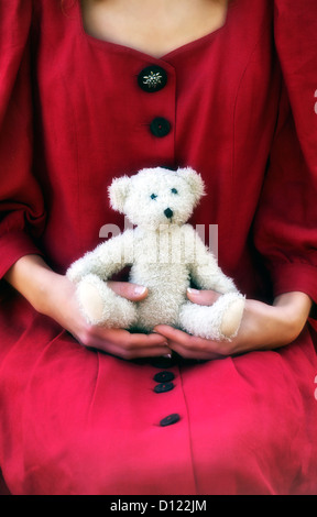 Une femme dans une robe rouge avec un ours en peluche sur ses genoux Banque D'Images