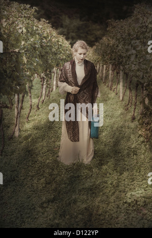 Une femme dans une robe de style édouardien blanc marche dans un vignoble Banque D'Images