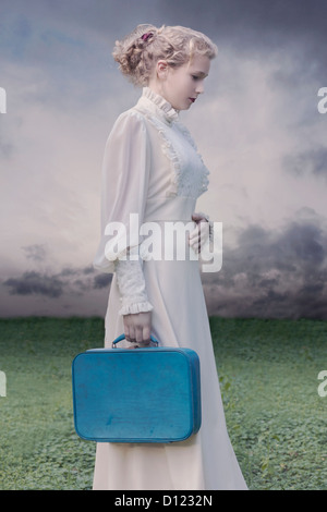 Une jeune femme en robe victorienne avec une valise bleue Banque D'Images