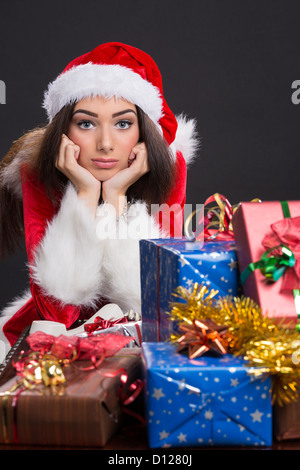 Portrait of a sad Santa girl avec cadeaux de Noël à l'avant. Banque D'Images