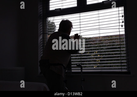 Hauts femme avec un déambulateur à la fenêtre d'un aveugle. Vue arrière, silhouette. Banque D'Images