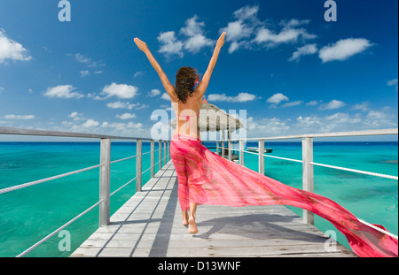 Polynésie Française, Tuamotu, Rangiroa Atoll, Woman Walking Down Ocean Pier Port Paréo Rose, Vue de derrière. Banque D'Images