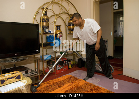 Mari qui prend soin de son épouse handicapée (jambe amputée) à la maison faisant l'aspirateur, Londres, Royaume-Uni. Parution du modèle image. Banque D'Images
