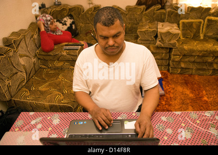 Mari qui prend soin de son épouse à la maison (handicapés assis, jambe amputée) utilise un ordinateur portable tout en femme regarde la télévision Banque D'Images